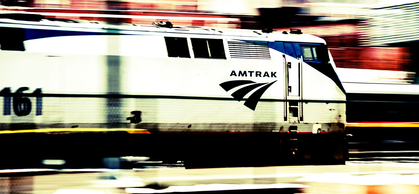 Image: PHOTO: A moving Amtrak passenger train pulling into a station. (photo via shanetrue / iStock Editorial / Getty Images Plus)