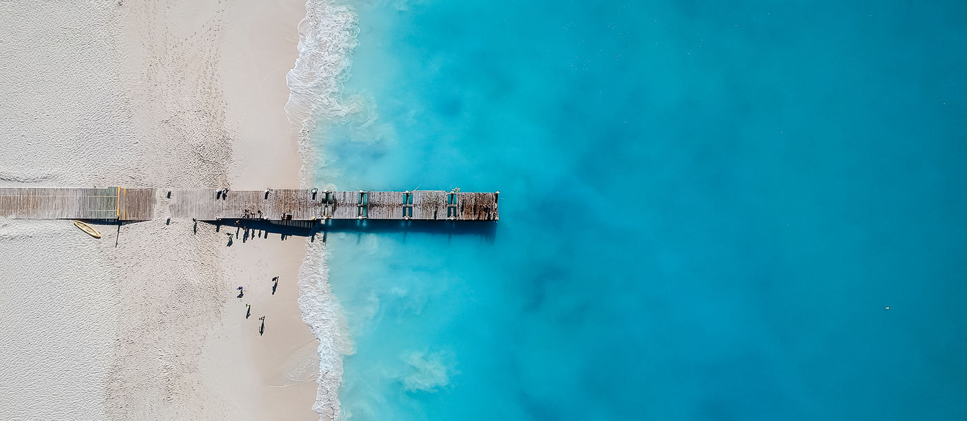 Drone photo of pier in Grace Bay, Providenciales, Turks and Caicos. The caribbean blue sea and white sandy beaches can be seen (photo via JoaoBarcelos / iStock / Getty Images Plus)